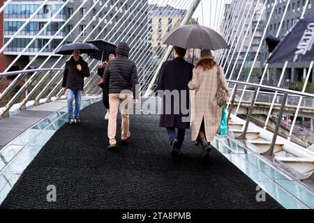 Cinque persone camminano in una giornata piovosa attraverso il ponte Zubizurri, uno dei ponti più famosi di Bilbao, in Spagna. Foto Stock