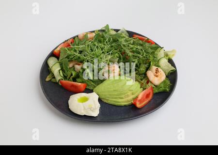 Insalata di gamberi, avocado, lattuga e pomodori ciliegini. Gustose foglie miste di verdure con gamberi grigliati in piatto nero su sfondo bianco. Foto Stock