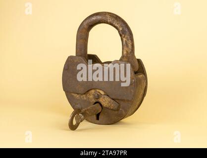 Un vecchio lucchetto arrugginito con una chiave al centro su uno sfondo beige. Foto Stock