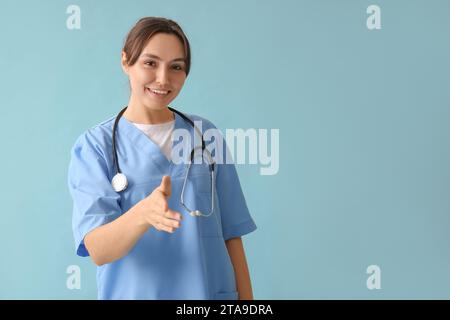 Bella medico femminile che estende la mano per la stretta di mano su sfondo blu Foto Stock