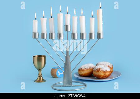 Menorah, ciambelle, tazza e dreidel per la celebrazione Hanukkah su sfondo colorato Foto Stock