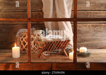 Manger con manichino di bambino e candele su sfondo di legno. Concetto di storia di Natale Foto Stock