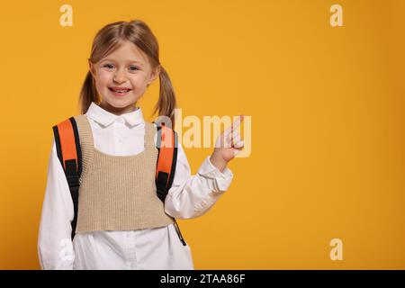 Studentessa felice con uno zaino che punta su qualcosa su sfondo arancione, spazio per il testo Foto Stock