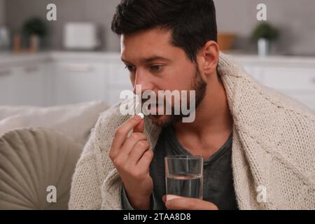 Uomo depresso con un bicchiere d'acqua che prende pillole antidepressive al chiuso Foto Stock