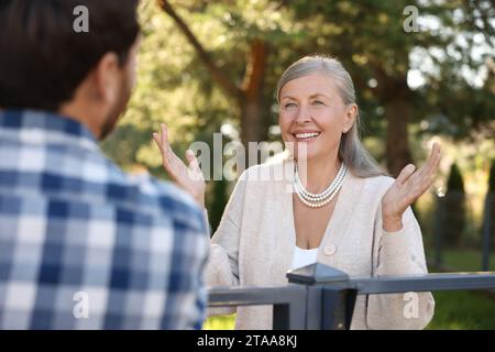 Rapporto amichevole con i vicini. Donna anziana felice che parla con un uomo vicino alla recinzione all'aperto Foto Stock