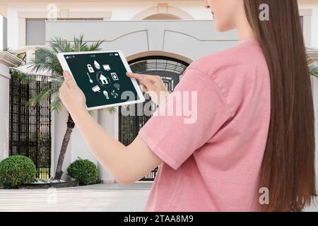 Donna che utilizza un sistema di controllo domestico intelligente tramite tablet vicino a casa all'aperto, primo piano Foto Stock