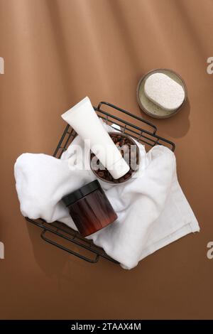 Vista dall'alto del tubo cosmetico e del vaso visualizzati sul cestello di plastica nero con asciugamano bianco e chicchi di caffè su sfondo marrone. Scena di mockup per la pubblicità Foto Stock