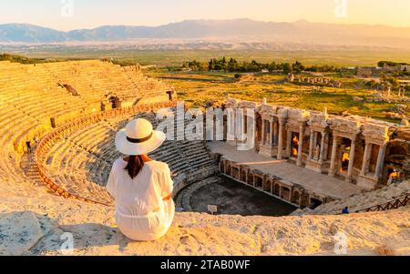 L'antica città di Hierapolis, Pamukkale, Turchia, è una giovane donna con un cappello che guarda il tramonto dalle rovine patrimonio dell'umanità dell'UNESCO. Donne asiatiche che guardano il tramonto al vecchio anfiteatro in Turchia Foto Stock