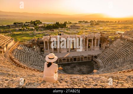 L'antica città di Hierapolis, Pamukkale, Turchia, è una giovane donna con un cappello che guarda il tramonto dalle rovine patrimonio dell'umanità dell'UNESCO. Donne asiatiche che guardano il tramonto al vecchio Anfiteatro in Turchia durante le vacanze Foto Stock