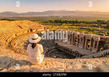 L'antica città di Hierapolis, Pamukkale, Turchia, è una giovane donna con un cappello che guarda il tramonto dalle rovine patrimonio dell'umanità dell'UNESCO. Donne asiatiche che guardano il tramonto al vecchio anfiteatro in Turchia durante il viaggio di vacanza Foto Stock