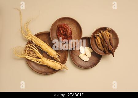 Vista dall'alto delle rare erbe esposte su piatti di legno - radici di ginseng, funghi ganoderma e ginseng rosso. Background beige per la pubblicità di prodotti e. Foto Stock