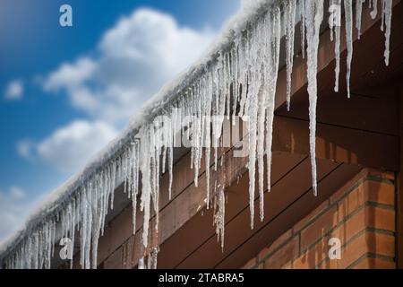 Ghiaccioli cristallini e luccicanti che si sono formati a causa delle condizioni climatiche gelide, appesi al bordo di una residenza in legno marrone Foto Stock