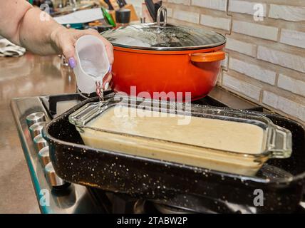 Lo chef prepara la torta per cuocere in un bagno d'acqua. Versare l'acqua nei piatti. Foto Stock