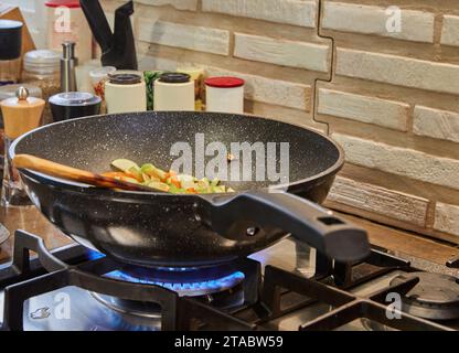 La padella con piatto e bastoncino di legno per mescolare viene cotta sul fuoco della stufa a gas. Foto Stock