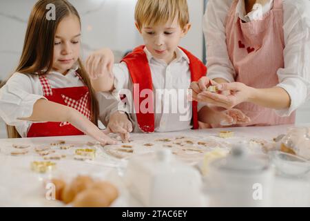 Primo piano delle mani dei bambini che tagliano i biscotti dall'impasto. Una bambina e un ragazzo stanno preparando dei biscotti di Natale. Foto Stock