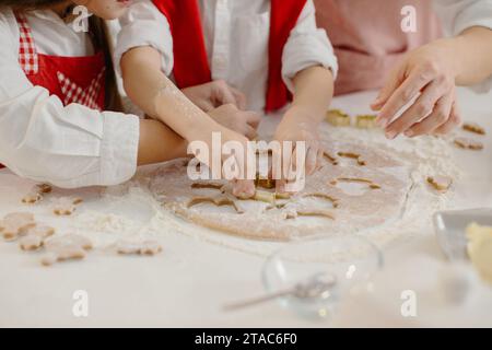 Primo piano delle mani dei bambini che tagliano i biscotti dall'impasto. Una bambina e un ragazzo stanno preparando dei biscotti di Natale. Foto Stock