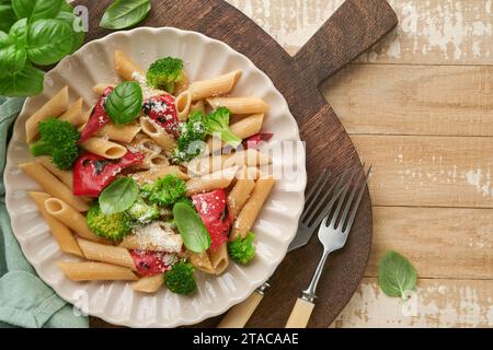 Penne per pasta integrale con broccoli e peperoni rossi grigliati e su un tavolo rustico in legno chiaro. Pasta vegana. Cucina tradizionale italiana Foto Stock