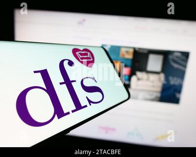 Telefono cellulare con logo della società di vendita al dettaglio britannica DFS Furniture plc di fronte al sito Web aziendale. Mettere a fuoco il display centrale sinistro del telefono. Foto Stock