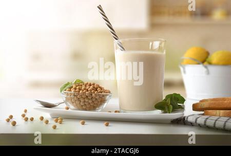 Latte vegetale di soia con bicchiere completo su panca da cucina con contenitore pieno di semi e pane tostato Foto Stock