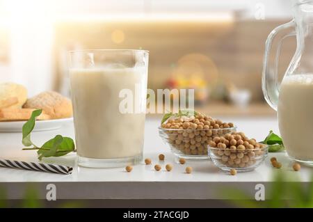 Colazione salutare con bevanda di soia vegetale in un bicchiere su una panca da cucina con contenitori pieni di semi e pane Foto Stock