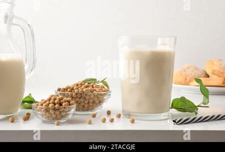 Colazione con latte e pane di soia su un tavolo bianco con ciotole piene di cereali e foglie vista dall'alto. Vista frontale. Foto Stock