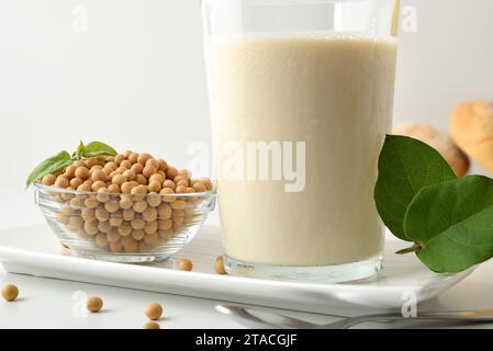 Dettaglio della colazione con latte e pane di soia su tavolo bianco con ciotola piena di cereali e foglie. Vista frontale. Foto Stock