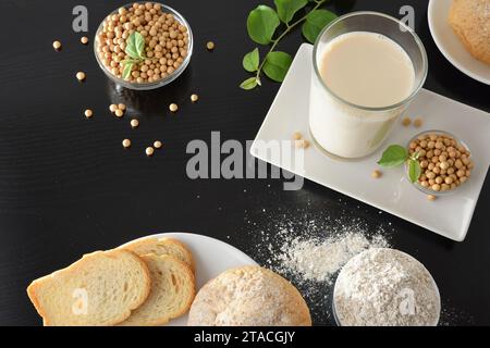 Colazione con latte di soia e pane di soia su tavola nera con ciotole piene di cereali e foglie. Vista dall'alto in alto. Foto Stock