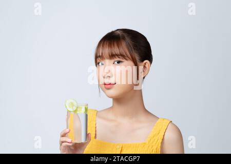 una bella giovane donna con un bicchiere d'acqua con fette di cetriolo isolate su bianco. Foto Stock