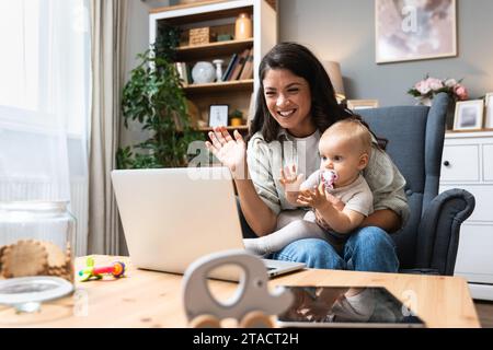 Resta a casa mamma che lavora in remoto sul notebook mentre si prende cura del suo bambino. Una giovane madre d'affari in congedo di maternità che cerca di diventare freelance vicino alla scrivania Foto Stock