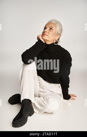 donna d'affari di mezza età sognante in un elegante abbigliamento casual, seduta su sfondo grigio Foto Stock