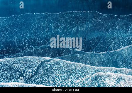 Sopra le onde del mare che si infrangono sulla spiaggia di sabbia nera in Islanda Foto Stock