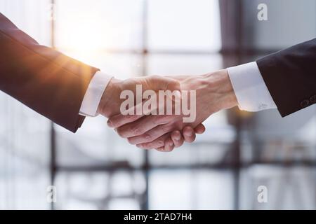 Uomini d'affari che scuotono le mani in piedi davanti alle finestre dell'ufficio Foto Stock