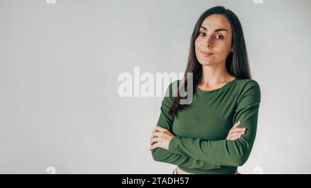 Splendida donna bruna sorridente e sicura di sé, vestita in modo informale. Foto in studio di una bella donna d'affari isolata contro un muro vuoto dello studio. Foto Stock