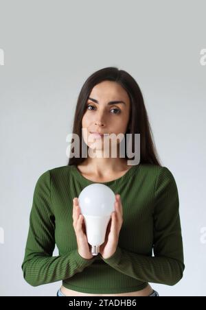 Ragazza con una lampadina a LED. Utilizzo di lampadine economiche ed ecologiche. Lampadina a risparmio energetico in mano alle donne. Affari creativi Foto Stock