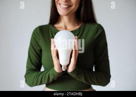 Ragazza con una lampadina a LED. Utilizzo di lampadine economiche ed ecologiche. Lampadina a risparmio energetico in mano alle donne. Affari creativi Foto Stock