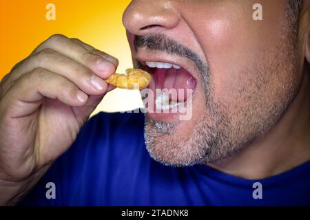 Primo piano di un uomo affamato che morde un gambero. Irresistibile desiderio di cibo. Sfondo giallo. Foto Stock