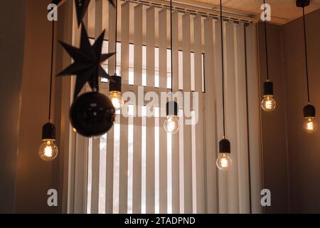 Le lampadine sui fili e le decorazioni dell'albero di Natale sono appese al soffitto di fronte alla finestra Foto Stock