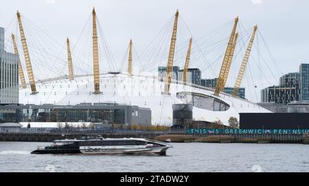 Un battello fluviale Uber passa davanti all'arena O2, edificio millenario su una riva del Tamigi, presso la penisola di Greenwhich, Londra, Inghilterra. Foto Stock