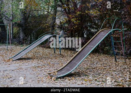 Due vecchi e pericolosi scivoli per bambini colorati in metallo nel cortile sovietico. Parco giochi a Bishkek, Kirghizistan Foto Stock