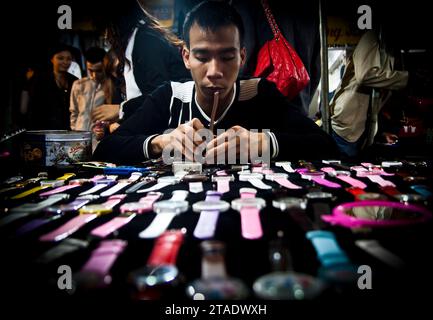 Un uomo prepara orologi da polso per la vendita al mercato notturno di Hanoi, in Vietnam Foto Stock
