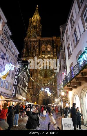 Gli amanti dello shopping riempiono le strade di Strasburgo, in Francia, di fronte alla Cattedrale di Notre Dame durante i mercatini di Natale annuali nella città orientale della Francia. I mercati sono uno dei più antichi d'Europa, essendo operativi da oltre 400 anni. Si stima che oltre due milioni di persone visiteranno la città durante la stagione di Yule del 2023. Foto Stock