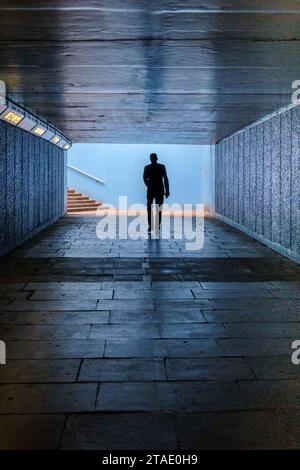 Silhouette di una persona che cammina in un sottopassaggio pedonale scuro verso gradini e luce del giorno. Foto Stock