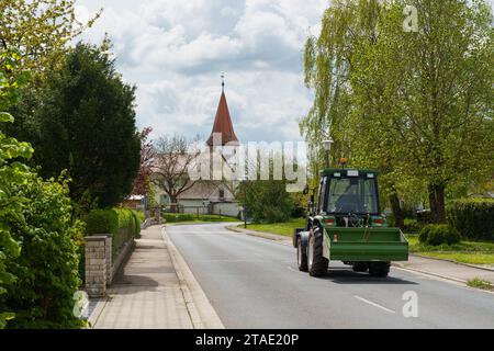 Feuchtwangen, Germania - 6 maggio 2023: Un trattore agricolo verde percorre la strada di una piccola città tedesca. Foto Stock