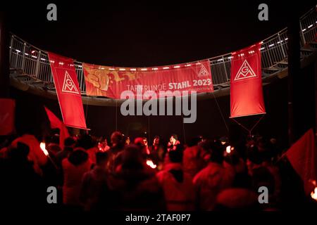 Duisburg, Germania. 30 novembre 2023. In occasione di una protesta nel corso dell'attuale contenzioso salariale, un cartello recita "Collective Bargaining round Steel 2023”. I sindacalisti delle acciaierie di Duisburg e le delegazioni dei rami circostanti simbolicamente suonano alla fine dell'obbligo di pace. I sindacalisti marciano con le torce dal Hüttenschenke di Hüttenwerke Krupp Mannesmann alla piattaforma panoramica di Tiger & Turtle a Duisburg. Credito: Fabian Strauch/dpa/Alamy Live News Foto Stock