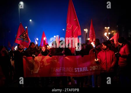 Duisburg, Germania. 30 novembre 2023. I partecipanti alla manifestazione sindacale IG Metall camminano verso la piattaforma di osservazione durante una protesta nel corso dell'attuale disputa salariale. I sindacalisti delle acciaierie di Duisburg e le delegazioni dei rami circostanti simbolicamente suonano alla fine dell'obbligo di pace. I sindacalisti fanno una marcia con fiaccolata dal Hüttenschenke di Hüttenwerke Krupp Mannesmann alla piattaforma panoramica di Tiger & Turtle a Duisburg. Credito: Fabian Strauch/dpa/Alamy Live News Foto Stock