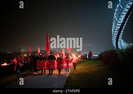 Duisburg, Germania. 30 novembre 2023. I partecipanti alla dimostrazione camminano verso la piattaforma di osservazione durante una protesta nel corso dell'attuale disputa salariale. I sindacalisti delle acciaierie di Duisburg e le delegazioni dei rami circostanti annunciano simbolicamente la fine dell'obbligo di pace. I sindacalisti fanno una marcia con fiaccolata dal Hüttenschenke di Hüttenwerke Krupp Mannesmann alla piattaforma panoramica di Tiger & Turtle a Duisburg. Credito: Fabian Strauch/dpa/Alamy Live News Foto Stock