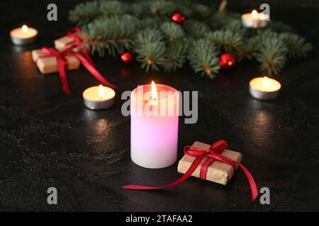 Composizione con candele in fiamme, regali di Natale e rami di abete su sfondo scuro Foto Stock