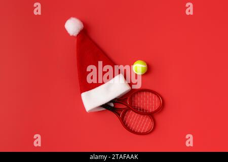 Composizione con mini racchette da tennis, palla e cappello da Babbo Natale su sfondo rosso Foto Stock