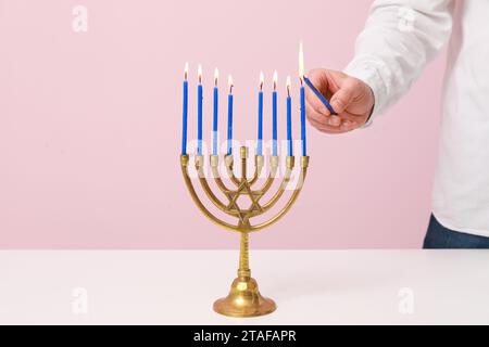 Uomo che accende candele in menorah su sfondo rosa, primo piano. Festa di Hanukkah Foto Stock