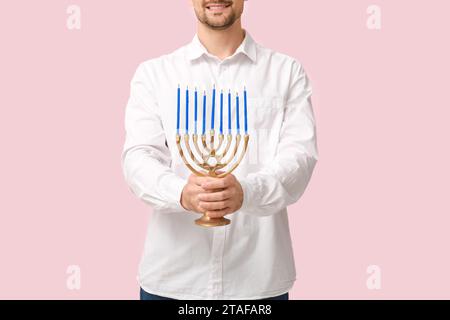 Uomo con menorah su sfondo rosa. Festa di Hanukkah Foto Stock